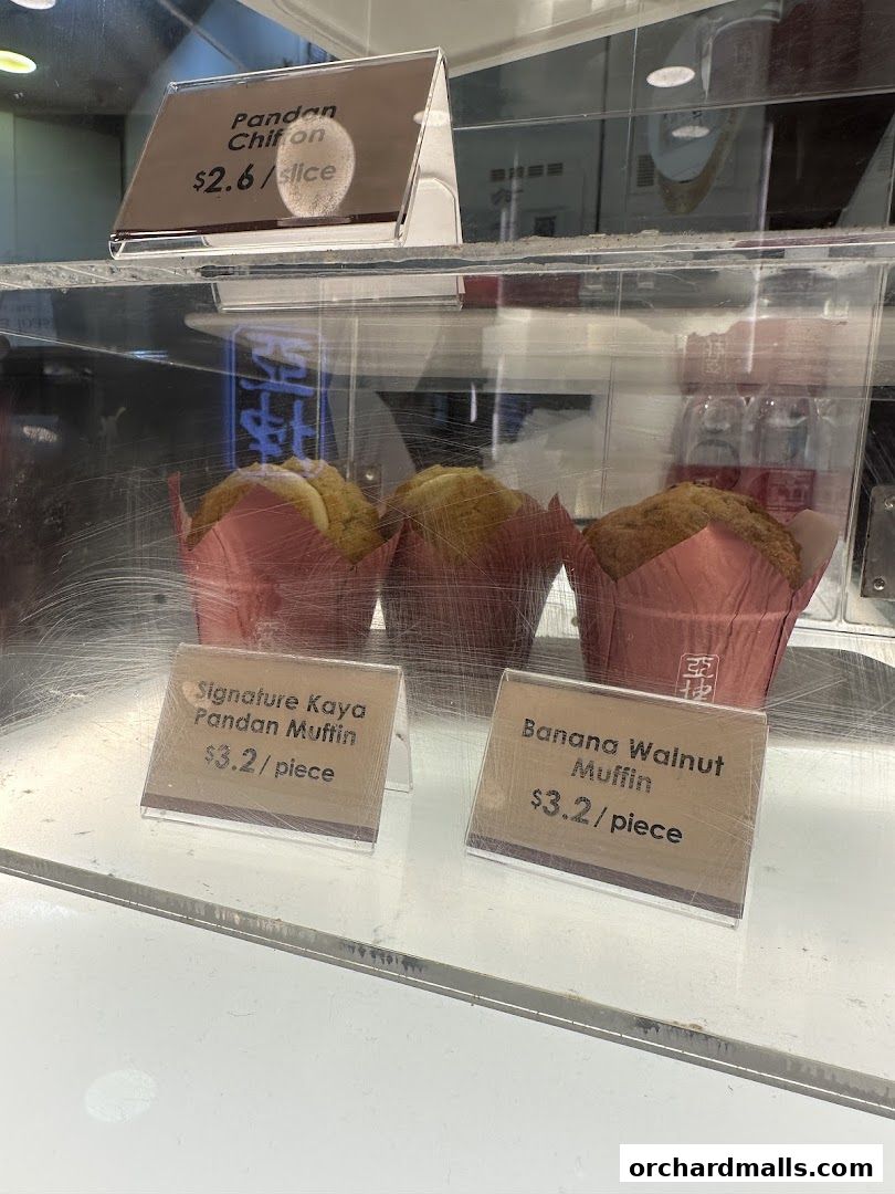 A display case featuring muffins and a slice of Pandan Chiffon cake.