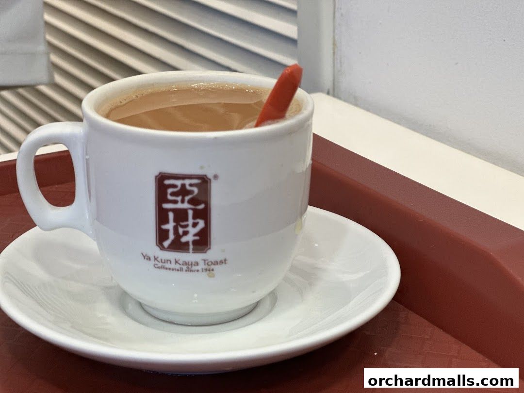 A close-up shot of a steaming cup of coffee with a red stirrer at Ya Kun Kaya Toast.