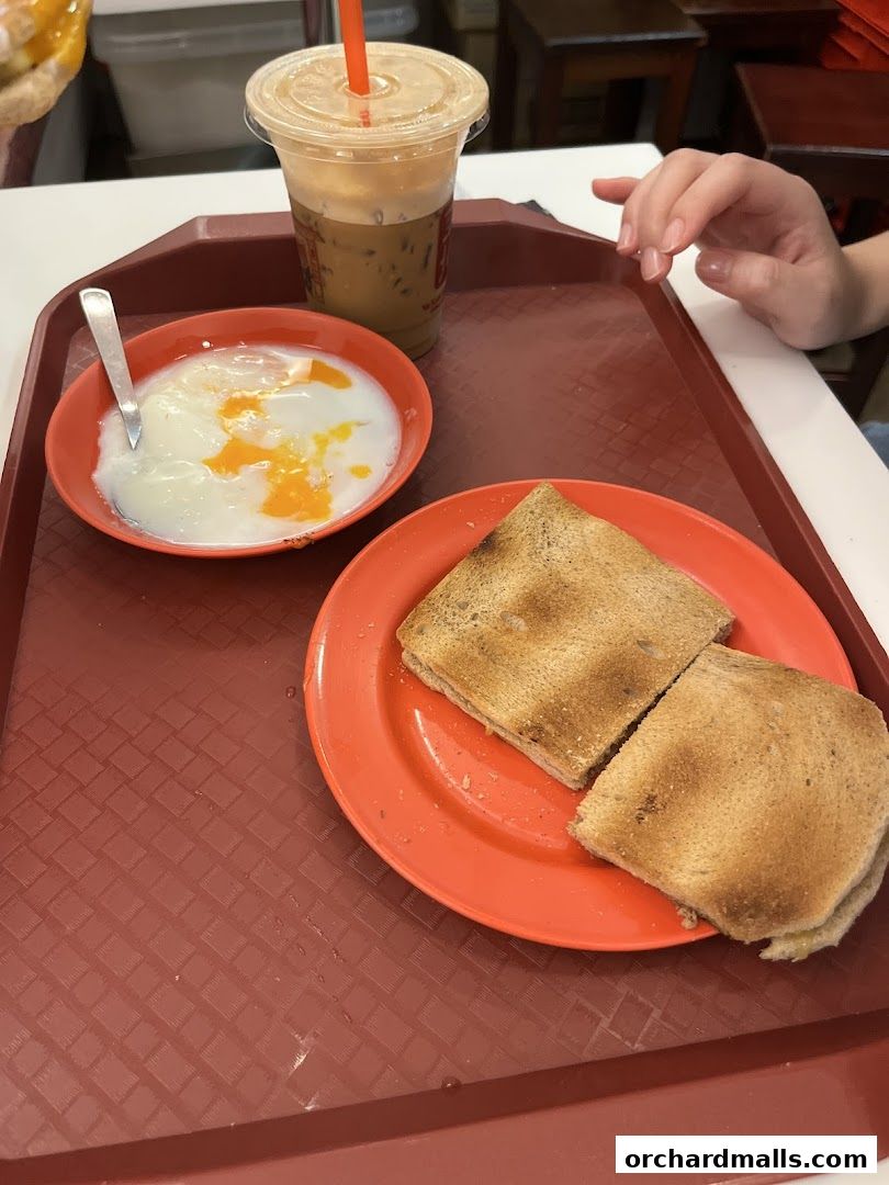 A tray with soft-boiled eggs, kaya toast, and iced coffee, ready to be enjoyed.