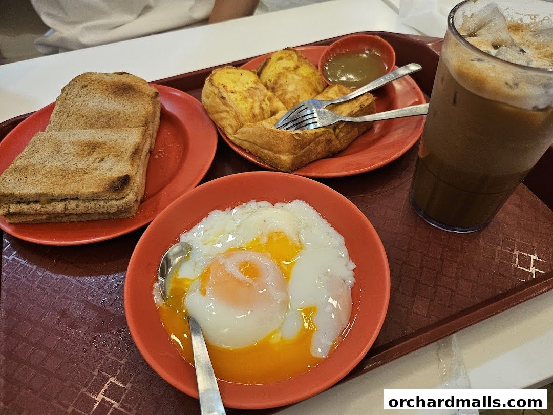 A tray of traditional Singaporean breakfast items including kaya toast, soft-boiled eggs, and iced coffee.