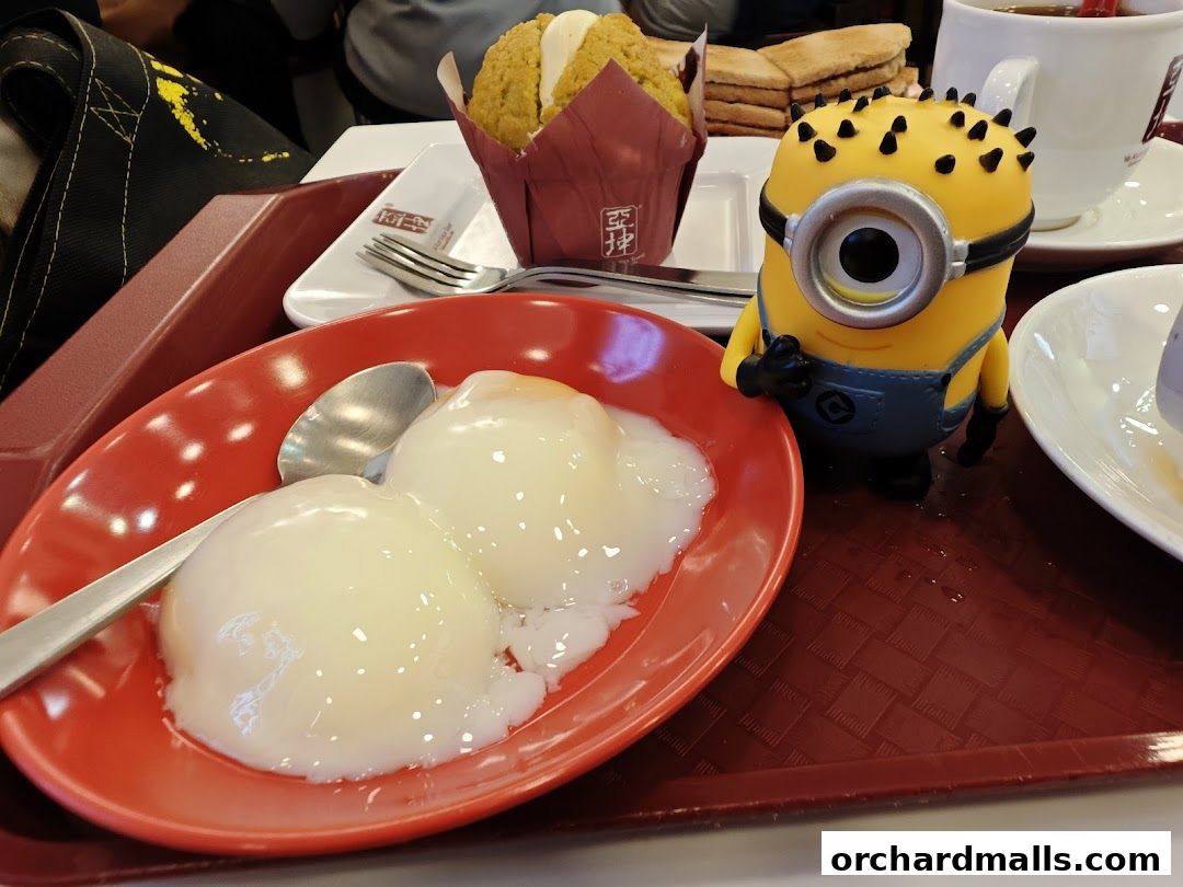 A tray of food from Ya Kun Kaya Toast, featuring soft-boiled eggs, a muffin, toast, and a Minion toy.
