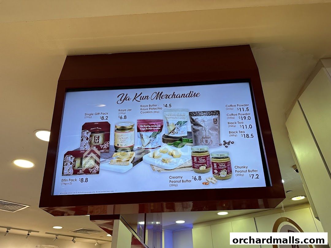 A digital menu board displaying Ya Kun merchandise, including kaya jars, cookies, coffee, and peanut butter.