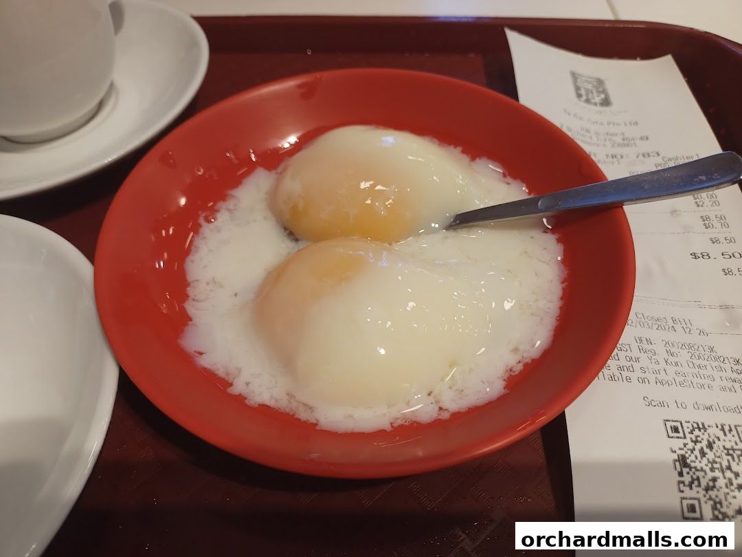 A close-up of two soft-boiled eggs in a red bowl with a spoon and a receipt.