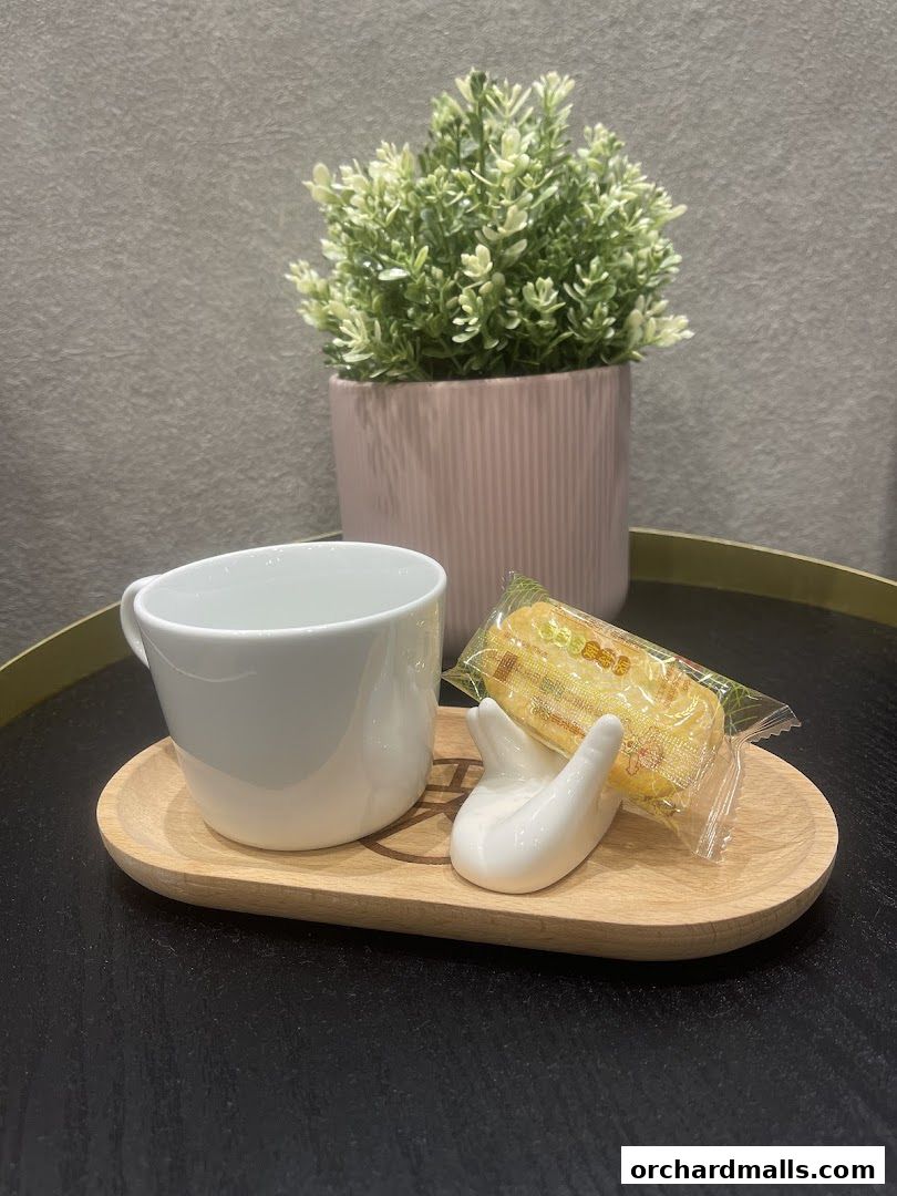 A white teacup and a packaged snack on a wooden tray with a decorative hand.