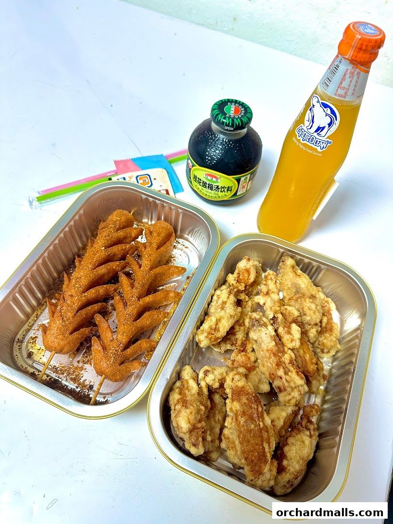 Two foil containers of fried chicken and skewers with a bottle of drink.