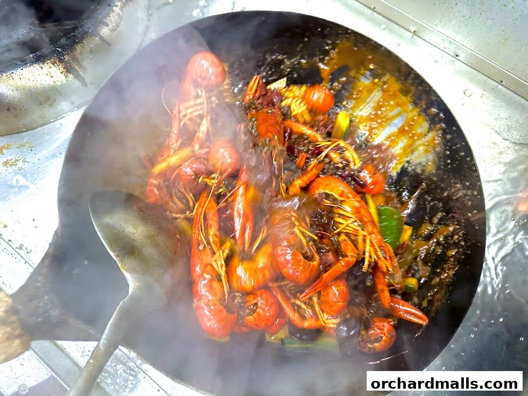 A wok filled with steaming crawfish and spices, being stirred with a large spatula.