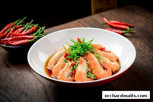 A bowl of succulent shrimp dish garnished with green onions and chili peppers.