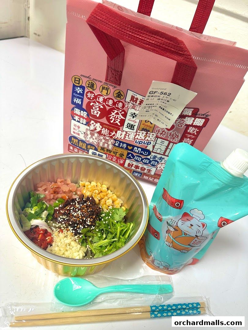A bowl of food with toppings, chopsticks, spoon, and a pink bag with Chinese characters.