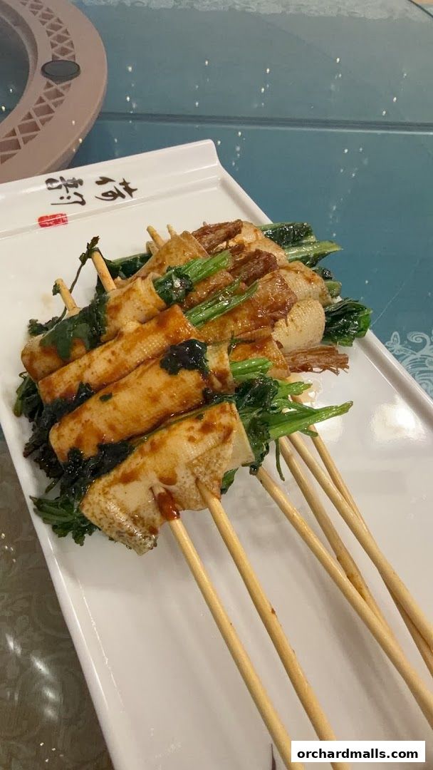 A platter of grilled skewers with tofu skin and vegetables, drizzled with sauce.