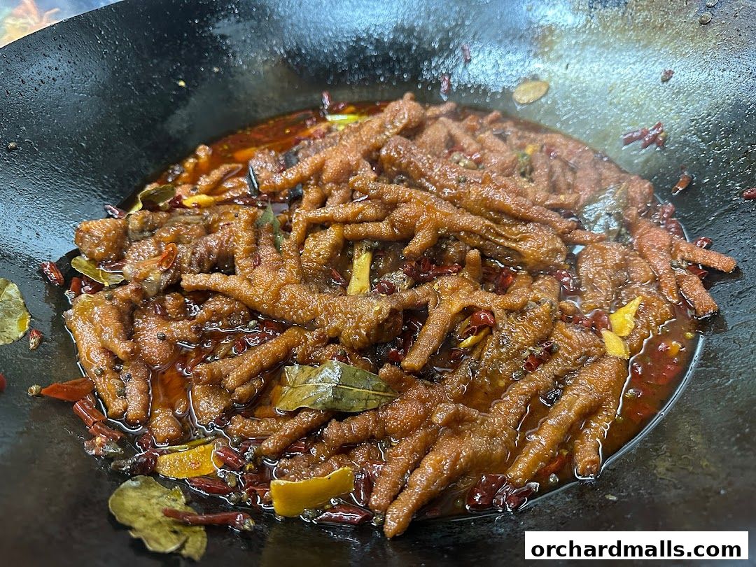 A close-up shot of braised chicken feet in a wok with spices and chili peppers.