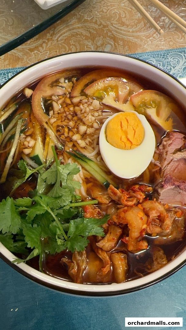 A close-up shot of a delicious bowl of noodles with egg, meat, vegetables, and herbs.