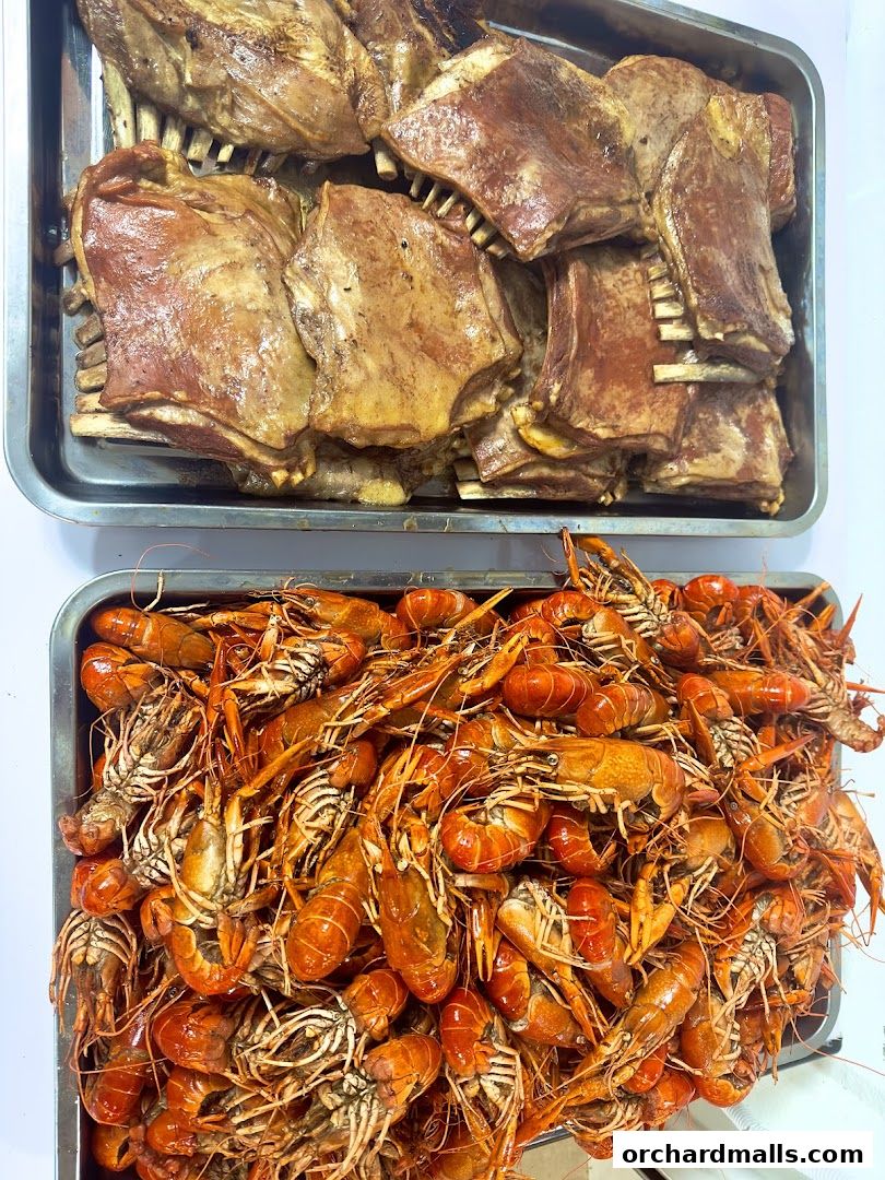 Two trays of food: one with grilled ribs, the other with cooked crawfish.