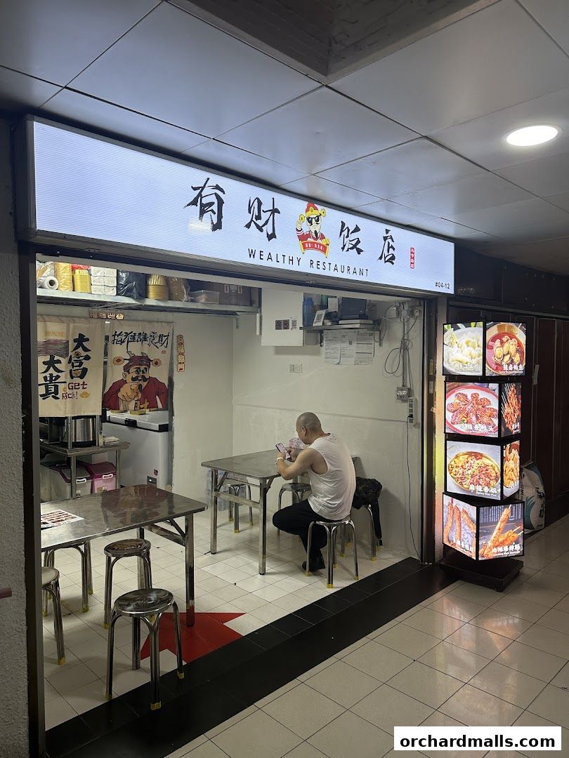 A man sits at a table in a small restaurant with a sign reading 'Wealthy Restaurant'.