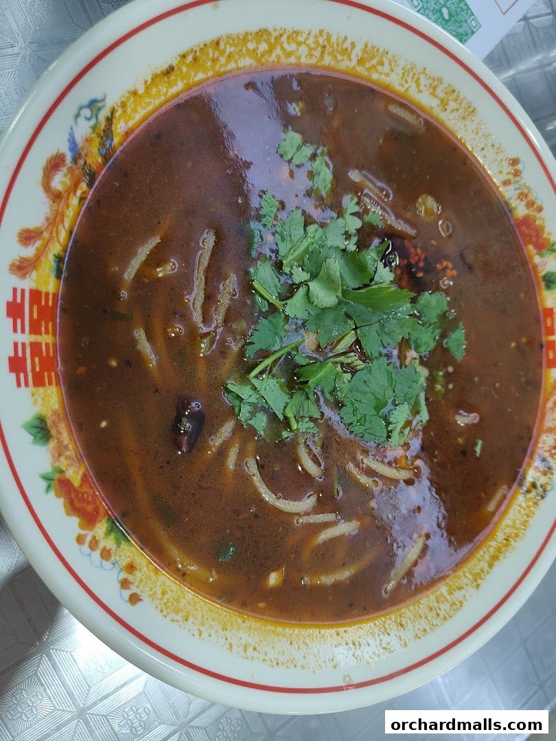 A close-up shot of a steaming bowl of spicy noodle soup topped with fresh cilantro.
