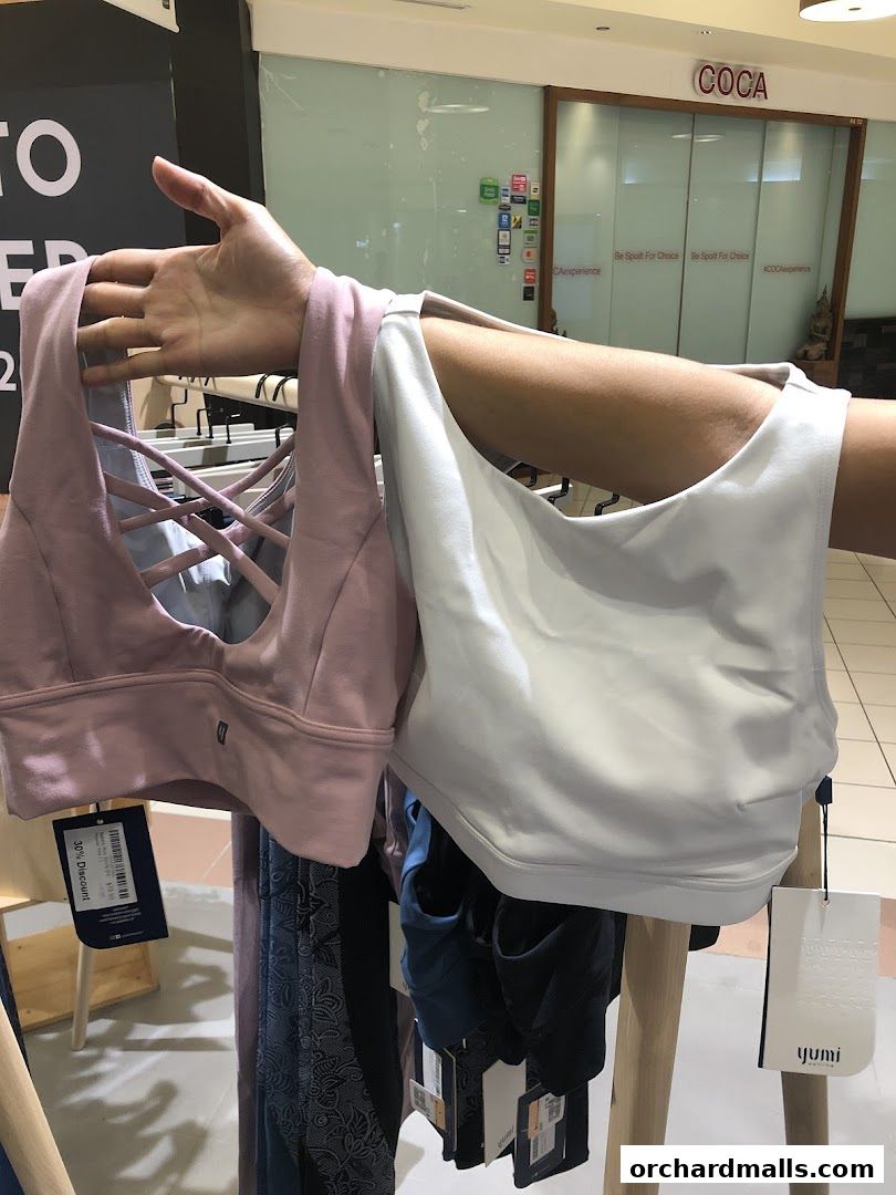 A person holds up two sports bras, one pink and one white, in a retail store.