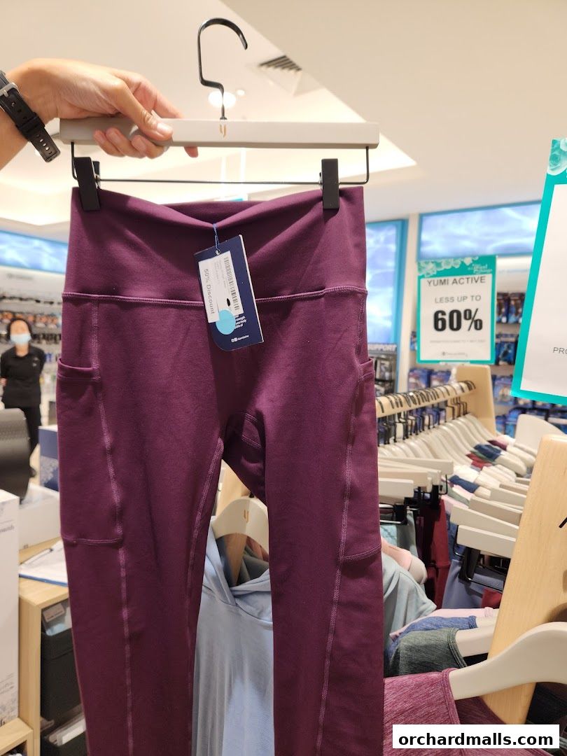 A hand holds up a pair of burgundy leggings with pockets, on display in a store.