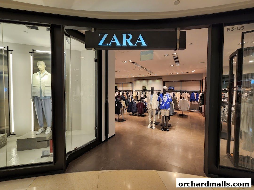 The entrance to a Zara clothing store with mannequins displaying outfits and racks of clothes inside.