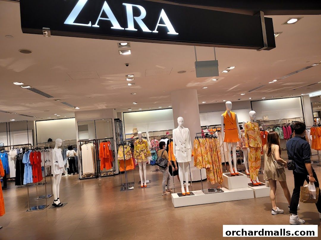 Interior view of a Zara store with mannequins displaying fashion apparel and shoppers browsing.