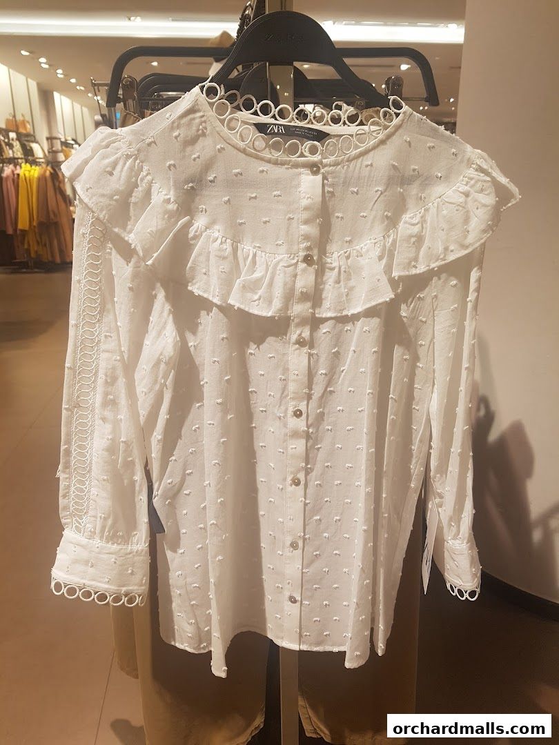 A white Zara blouse with ruffled details and decorative circular cutouts on the collar and cuffs.