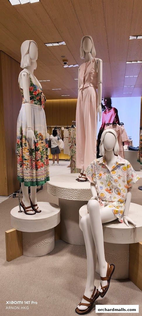 Mannequins display summer fashion outfits, including dresses and coordinated sets, in a well-lit store.