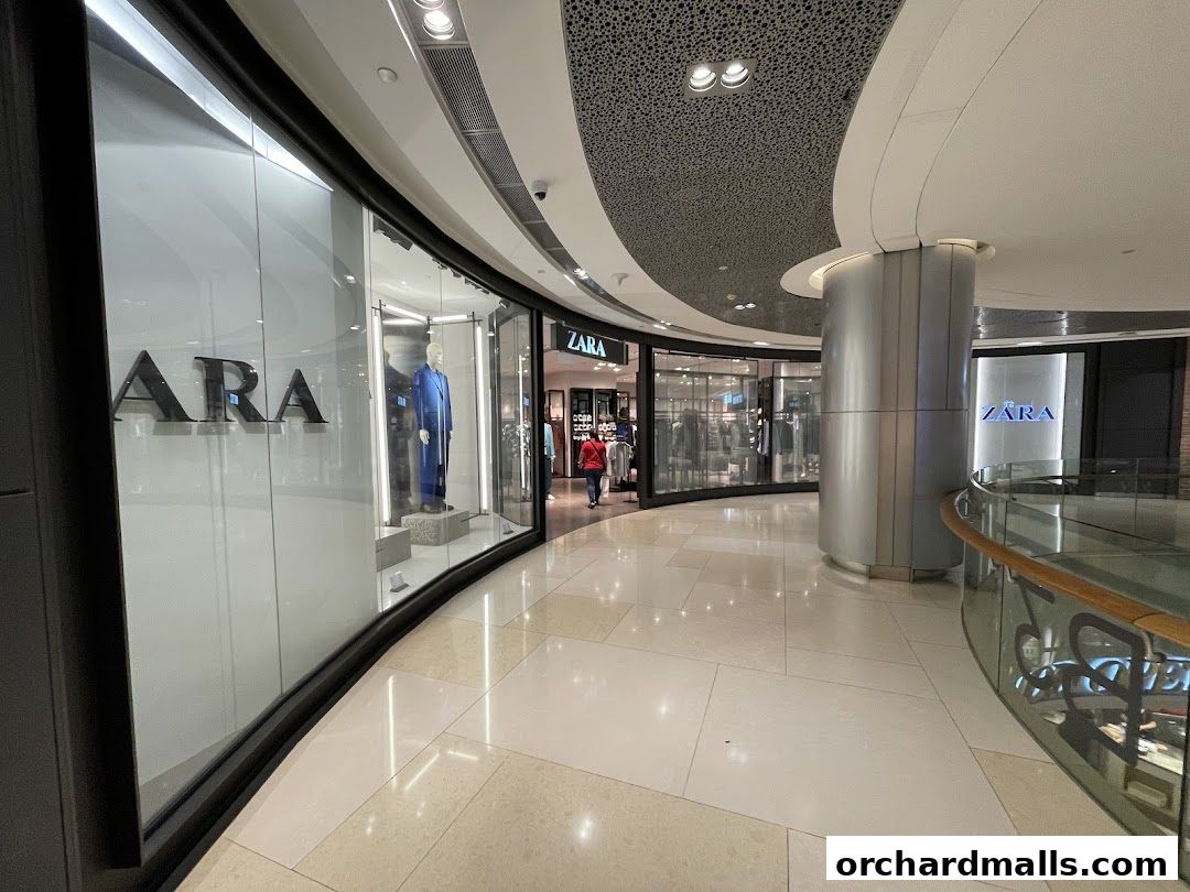 The exterior of a Zara store in a modern shopping mall, showcasing mannequins in the window.