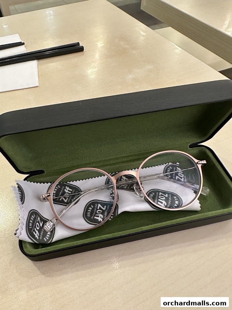 A pair of rose gold round eyeglasses in a green case with a cleaning cloth.