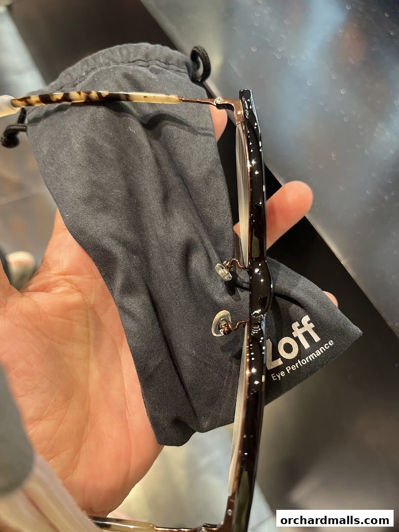 A hand holds a pair of stylish eyeglasses with a branded cleaning cloth.