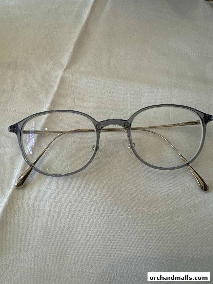 A pair of stylish, round, grey-framed eyeglasses with thin gold temples rests on a textured white surface.