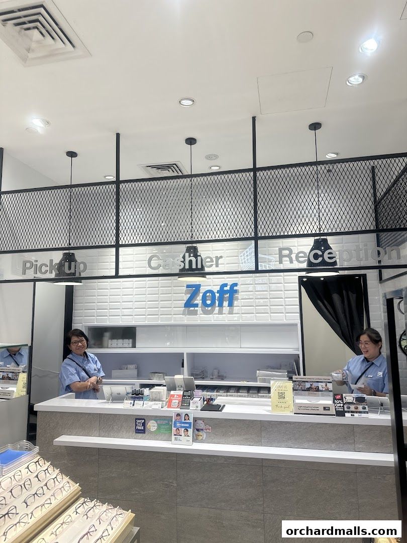 Two staff members stand behind the counter at Zoff, an optical shop, with displays of glasses visible.