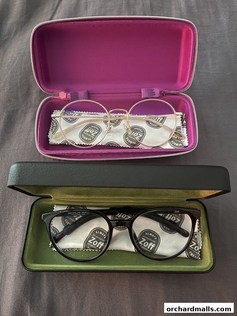 Two pairs of Zoff eyeglasses, one gold and one black, displayed in their cases.